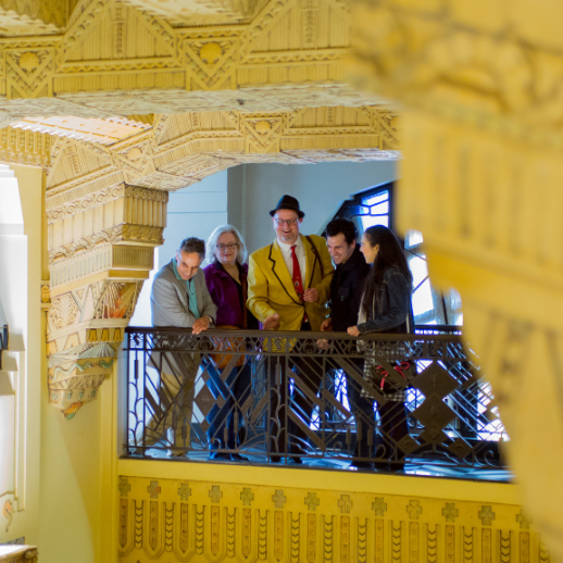 A group of 5 look down from the Marine Building balcony with beautiful Art Deco details all around