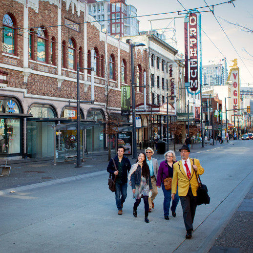 A group of 5 people walk across Granville Street with iconic signs "Orpheum" and "Vogue" in the background