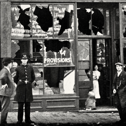 A black and white photo of a Gastown store with the windows broken, a police officer stands by as a young girl peeks out of the store