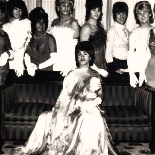A black and white photo of several drag queens posing for a photo in glamourous pageant-style dresses
