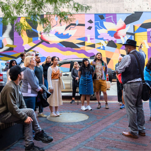 a storyteller stops his group in front of colourful mural