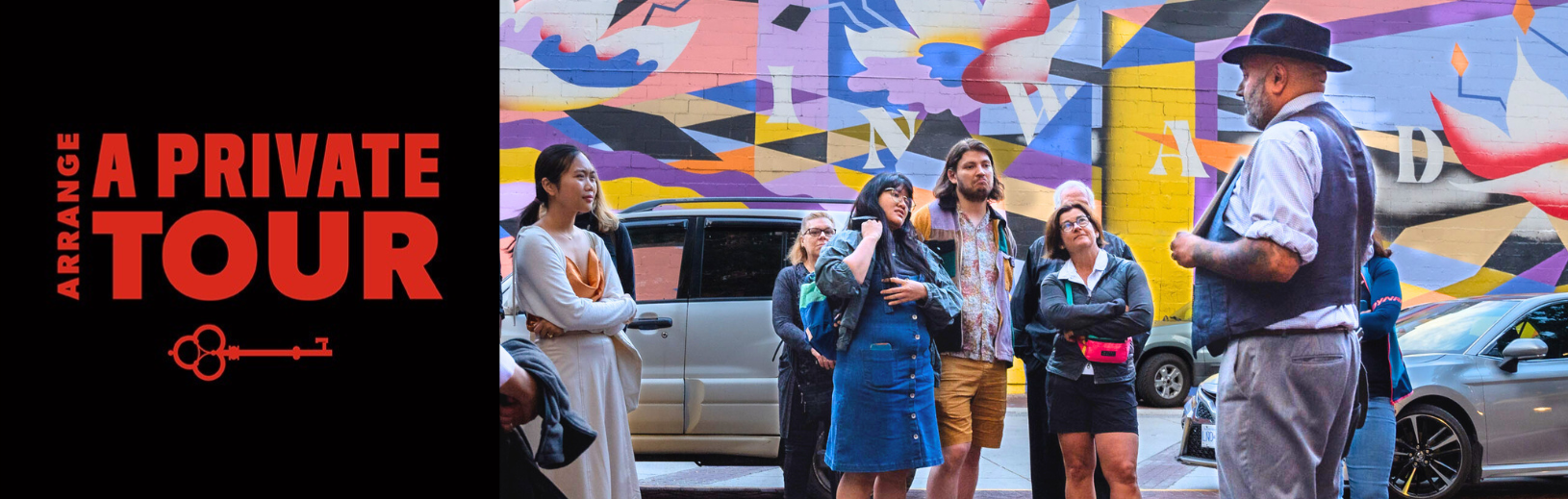 a man shows and image to his tour group in front of a colourful mural